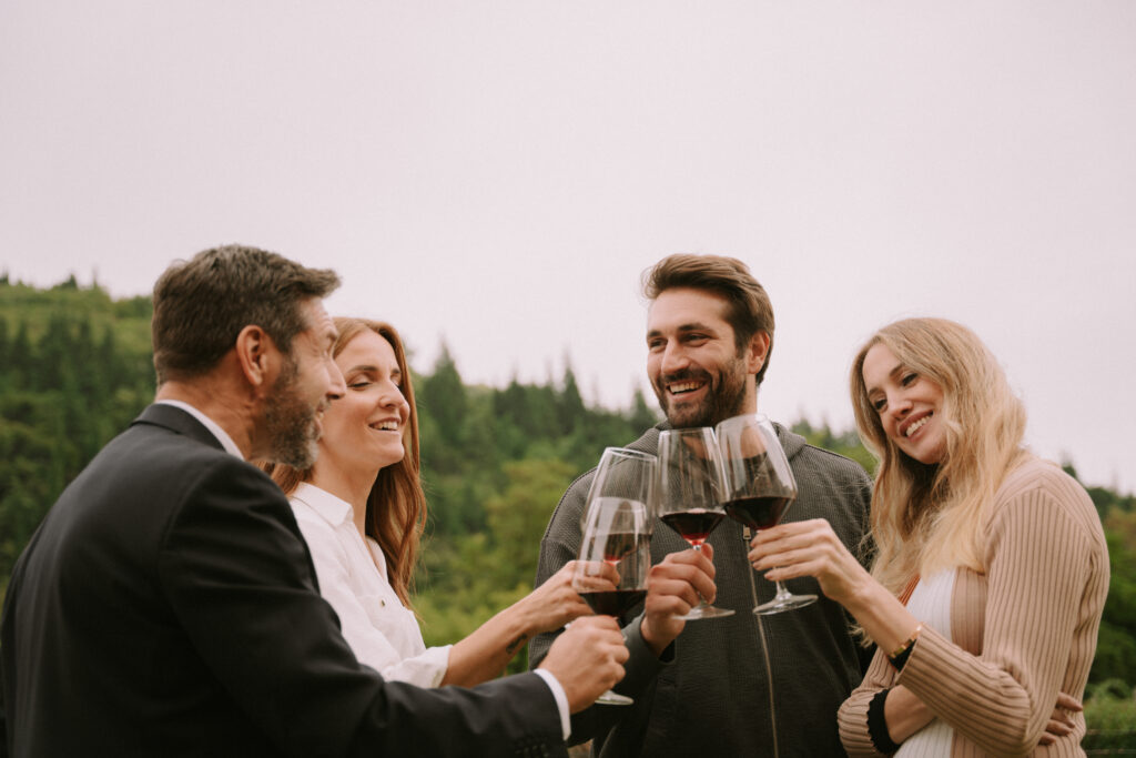 Cesari Esperienze Back To Classics two men and two women cheering outdoors with nature in the background and toasting with glasses filled with red wine