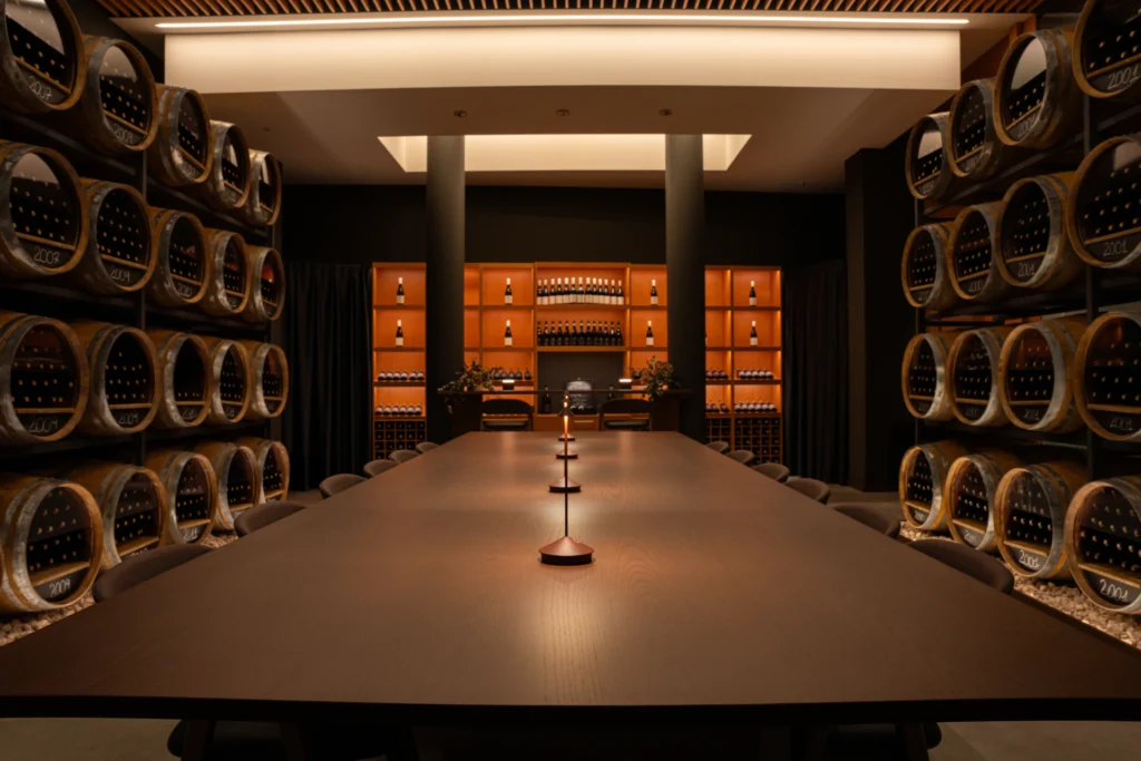 elegant empty winery setting with a walls of barrels on the side and a huge table with seats, the lights are lim and warm