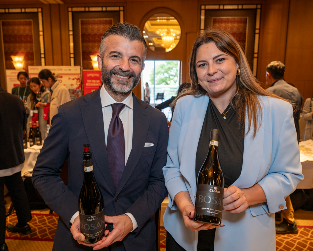 Two persons smiling and standing with a bottle of Bosan Riserva by Cesari in a wine tasting room