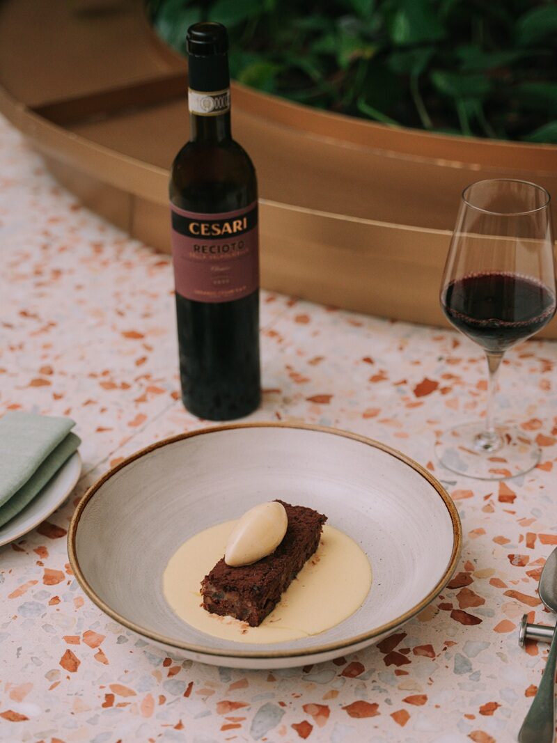 Recioto della Valpolicella Cesari on a dining table with a marble surface, and a gourmet dessert with chocolate and cream on a white plate and minimal mise en place