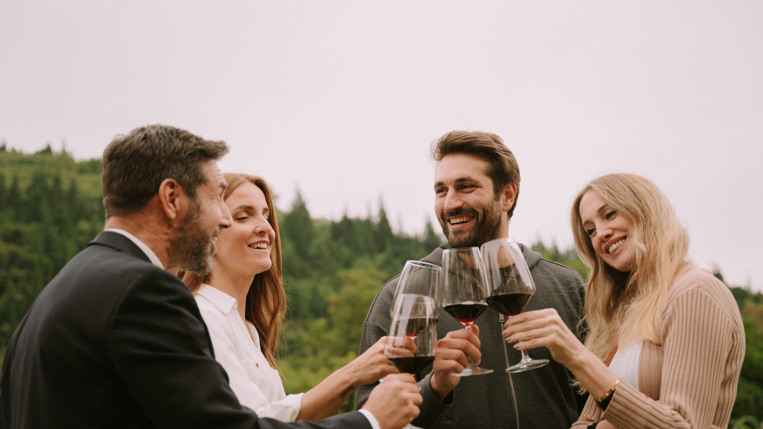 Cesari Esperienze Back To Classics two men and two women cheering outdoors with nature in the background and toasting with glasses filled with red wine