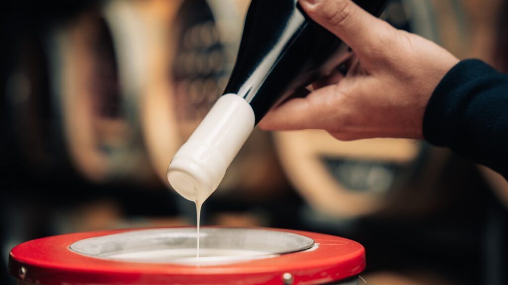 collezionare Amarone della Valpolicella_hand dipping the tip of a bottle into white wax to create a wax seal inside a wine cellar