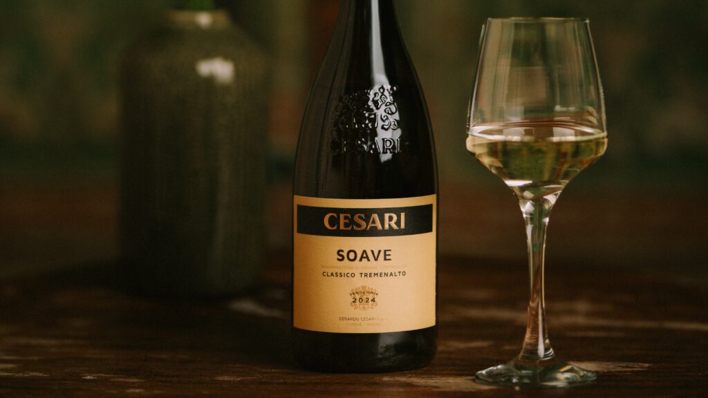 Soave classico cesari close-up shot of bottle of white wine with yellow label, beside a glass of white wine and with a blurred background